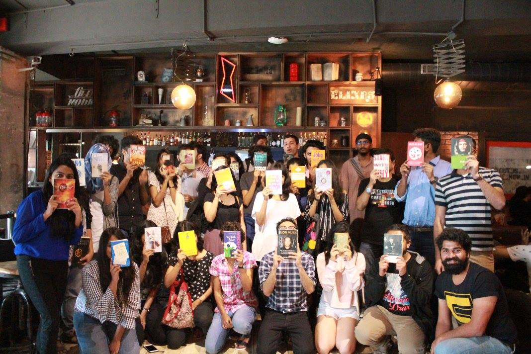 A room full of Sip and Swap attendees holding books in front of their faces inside a Mumbai cafe